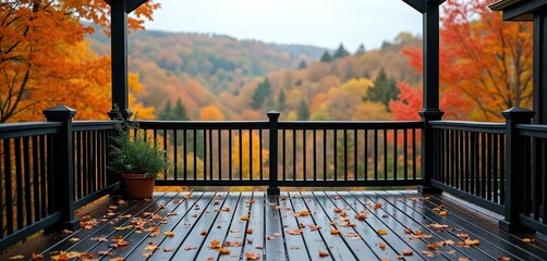 Fototapeta premium Backyard porch with black railings, wet wooden floor after rain. Fallen autumn leaves cover deck with scenic view of colorful forest. House patio overlooks beautiful hillside with vibrant orange,