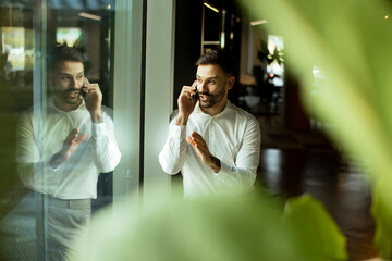 Businessman discussing phone call while standing in modern office space