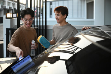 A young Asian gay couple happily cleans their car together, sharing smiles and teamwork during a relaxing evening routine