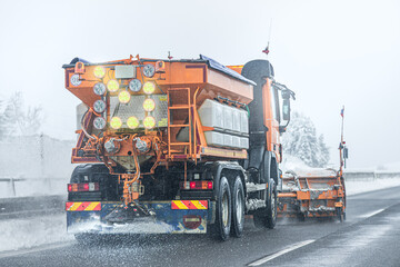 Naklejka premium Snow plow sprinkles highway with road salt in freezing weather.