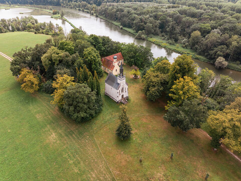 Historische Kapelle und Kirche am Flussufer, umgeben von Wald und Wiesen &ndash; Luftaufnahme