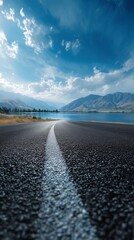 Scenic Asphalt Road Curving Through Mountain Valley With Lake and Rugged Peaks Under Clear Sky