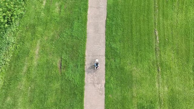 Top-down aerial view of a young woman riding a bicycle on a winding path in a green park
