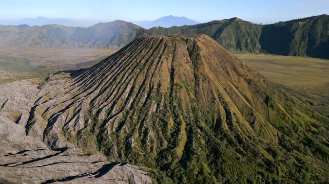 Cinematic aerial view of Mount Batok on sunny day near Mount Bromo. Rugged volcanic textures and warm morning light in East Java, Indonesia.