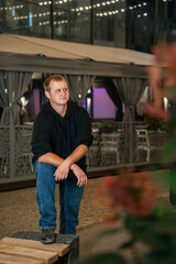 A young man in a black hoodie and blue jeans stands confidently outdoors at night