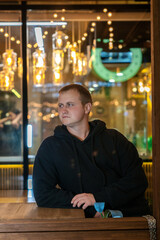 Pensive man in a black hoodie sits by a wooden table at night