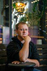 Man in a black hoodie sits thoughtfully