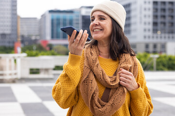Woman holding smartphone close to mouth while recording voice message on paved plaza, copy space
