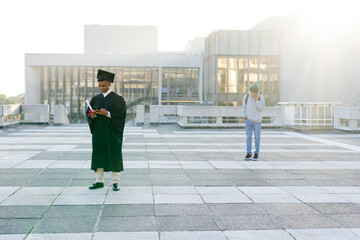 Adult male peers using phones while holding diploma in gown on rooftop terrace, copy space