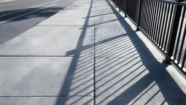 A smooth sidewalk slab with evenly spaced repeating railing-shadow lines forming calm geometric minimalism