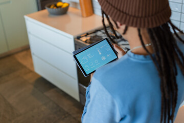 Tablet displaying smart climate and weather controls on countertop near stove, with bowl of fruit