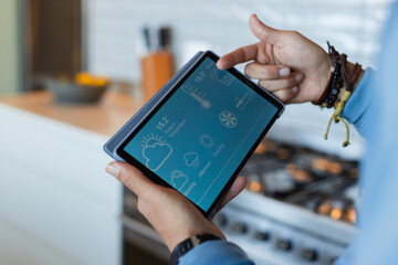 Tablet showing thermostat and weather being held over counter beside stovetop tools and lemon bowl