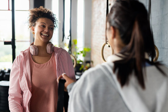 African American client smiling, taking band from Asian trainer beside rings in gym, copy space