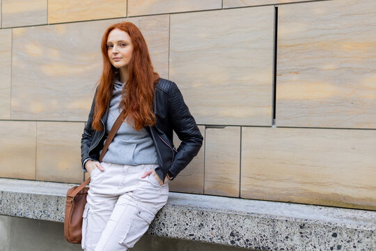 White woman leaning against bench carrying crossbody satchel before tiled wall, copy space