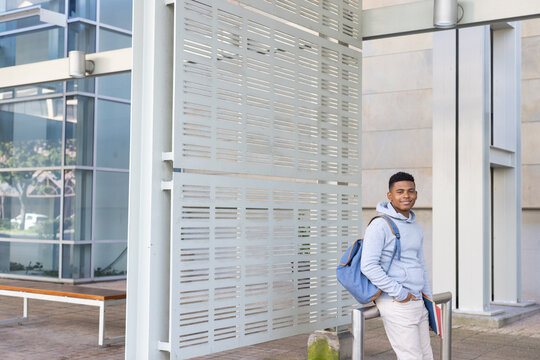 African American male student leaning on railing at campus wearing blue backpack, copy space