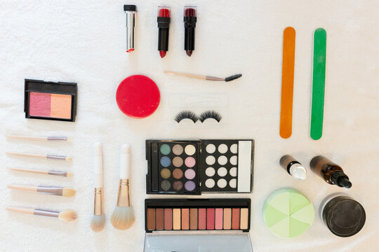Makeup tools lying in flat lay on white cloth, featuring palettes, brushes, lipsticks, nail files