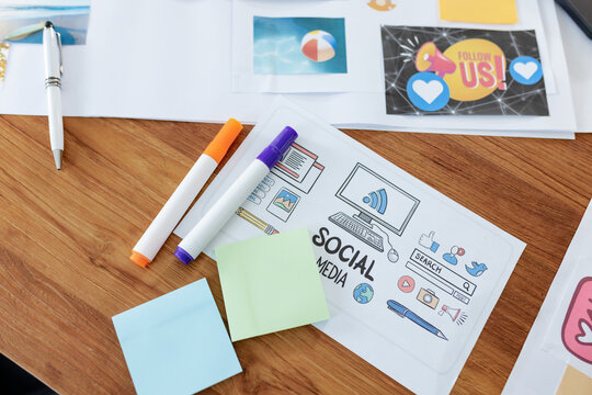 Sheet featuring SOCIAL MEDIA icons is sitting on wooden desk with markers and sticky notes nearby