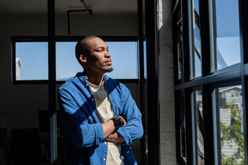 African American man wearing smartwatch and gazing at cityscape through loft windows in workspace