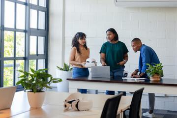 Diverse coworkers using VR controllers to test virtual reality headset at office table with laptop