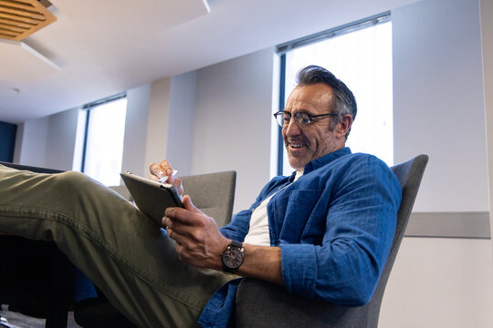 Man leaning back in chair while using stylus on tablet in office lounge, copy space