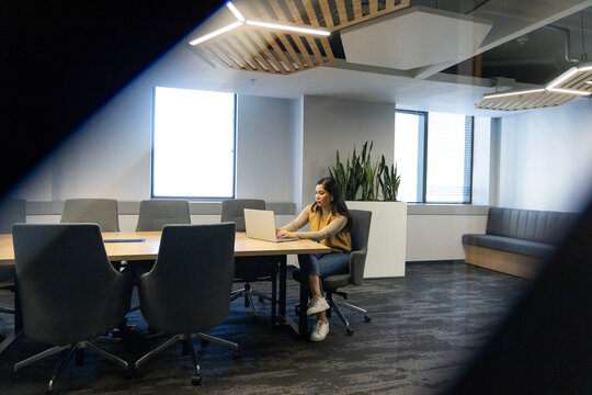 Mid adult Hispanic or Latino woman typing on laptop at meeting table, swivel chairs and planter