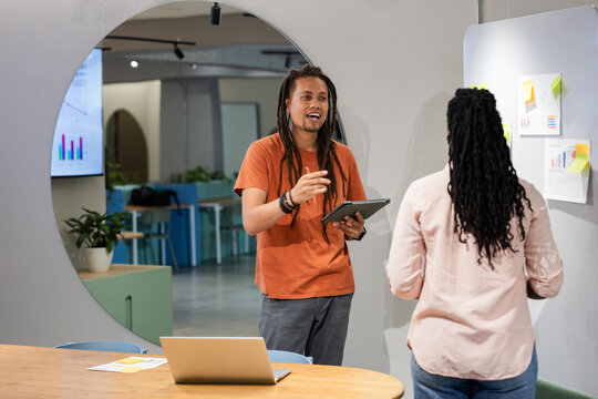 African American colleagues discussing strategy at modern office, using tablet and silver laptop