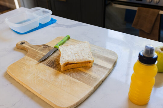 White bread sandwich is sitting on wooden cutting board on marble-look counter, knife near