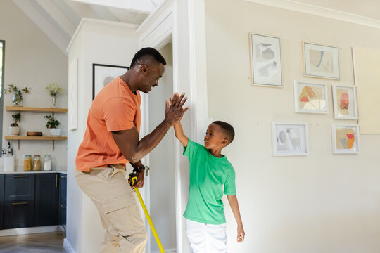 African American father and son high-fiving in hallway by doorway, man holding yellow tape measure
