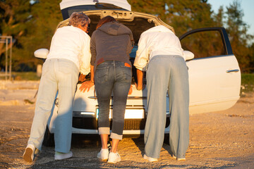 Three women looking under the hood of a car