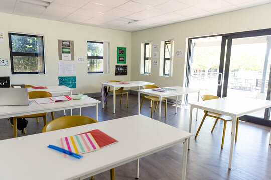 Foreground white desk holding striped multicolored notebook and two blue pens, classroom