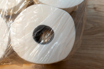 Rolls of toilet paper wrapped in plastic on a wooden surface, demonstrating practical household products. Ideal for marketing in hygiene, cleaning, and convenience sectors.