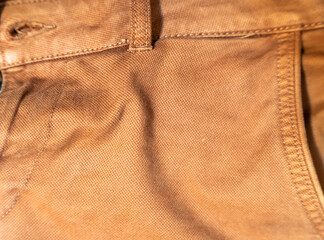 Close-up of brown fabric texture from denim pants showcasing stitching details and color variations. Ideal for fashion industry, apparel design, and textile marketing.