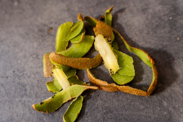 Close-up of sliced kiwi peels on a dark surface. The vibrant green and brown layers create an interesting texture. Ideal for food-related content, health, and culinary topics.