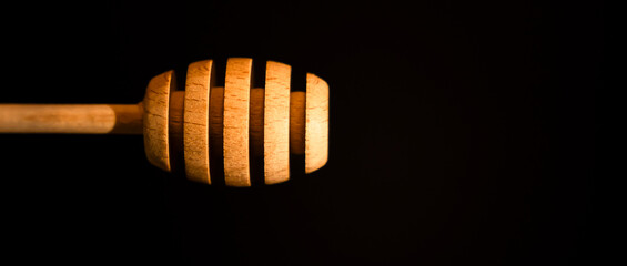 A wooden honey dipper stands against a dark background, showcasing its unique design with grooves. Ideal for food photographs, product advertisements, and culinary presentations.