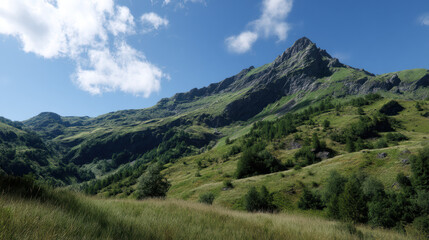 Obraz premium A picturesque mountain peak rises majestically against a vibrant blue sky with scattered clouds, overlooking lush green meadows and forested slopes in summer.