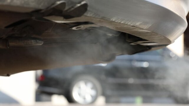 Close-up of a car exhaust pipe emitting white smoke and dripping water. Vehicle tailpipe releasing fumes and carbon dioxide pollution while the engine idles.


