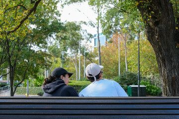 A couple sitting in a city park, spending time together in a peaceful outdoor environment with green trees and natural light.