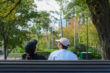 A couple sitting in a city park, spending time together in a peaceful outdoor environment with green trees and natural light.