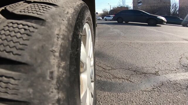 Low angle close-up of car wheel rolling on asphalt road in the city. Detailed view of tire tread and rim moving on the street during daytime traffic.

