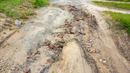 Washed-out dirt road after heavy rains with traces of water, old bricks, stones, gravel and sand.