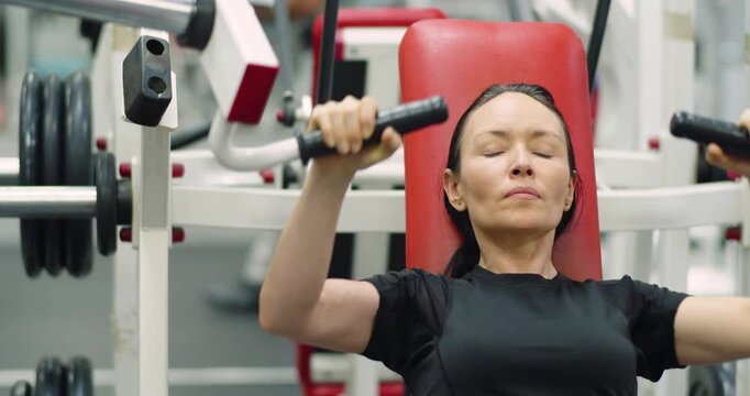 Slow motion 4k footage. A focused middle-aged woman powers through her bench press workout on the hammer machine, showcasing strength and determination in every controlled movement.