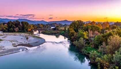 Serene river landscape at sunset with colorful sky transitioning from purple to orange, winding through lush forest and flanked by distant mountain ranges, sandy riverbank visible on one side.