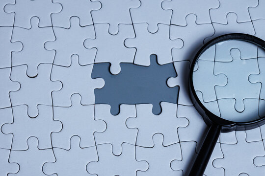 A magnifying glass placed on a white puzzle with a puzzle gap, identifying the root cause and finding a solution for the problem solving concept in business, corporate, or education