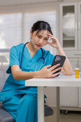 Healthcare nurse in scrubs looks worried while reading phone, burned out and emotionally drained at hospital workstation - female -