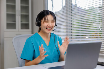 Asian medical professional having a telehealth video call, wearing scrubs and headset, providing remote consultation services