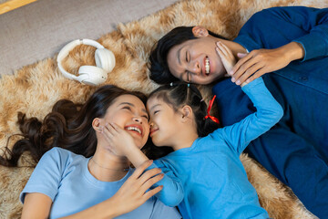 Happy Asian family laughing, cuddling, and lying together on a fluffy rug at home, cherishing moments of warmth and connection