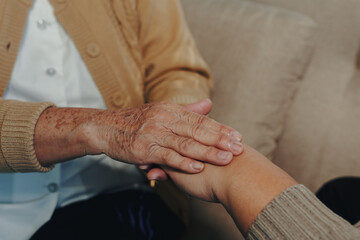 Senior woman's wrinkled hand gently covering a younger person's hand, symbolizing care, protection, and assistance between generations