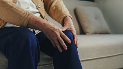 Elder woman suffering from chronic knee pain due to arthritis, holding her leg in discomfort,...