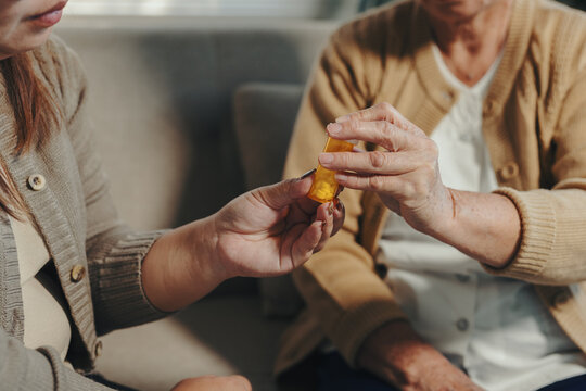 Caregiver's hands assisting an elderly woman in taking medication from a pill bottle, providing health support at home - Powered by Adobe