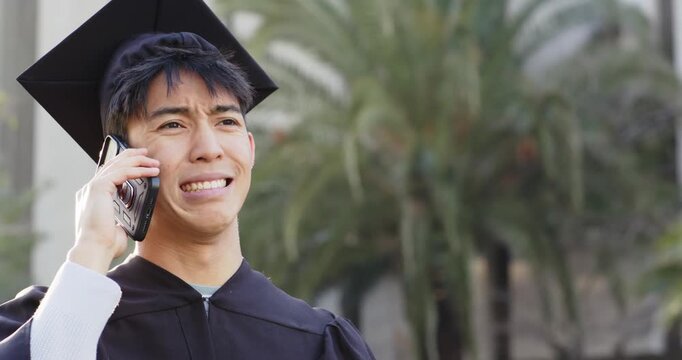 Receiving phone call, Asian man in mortarboard talking on smartphone on campus processing bad news